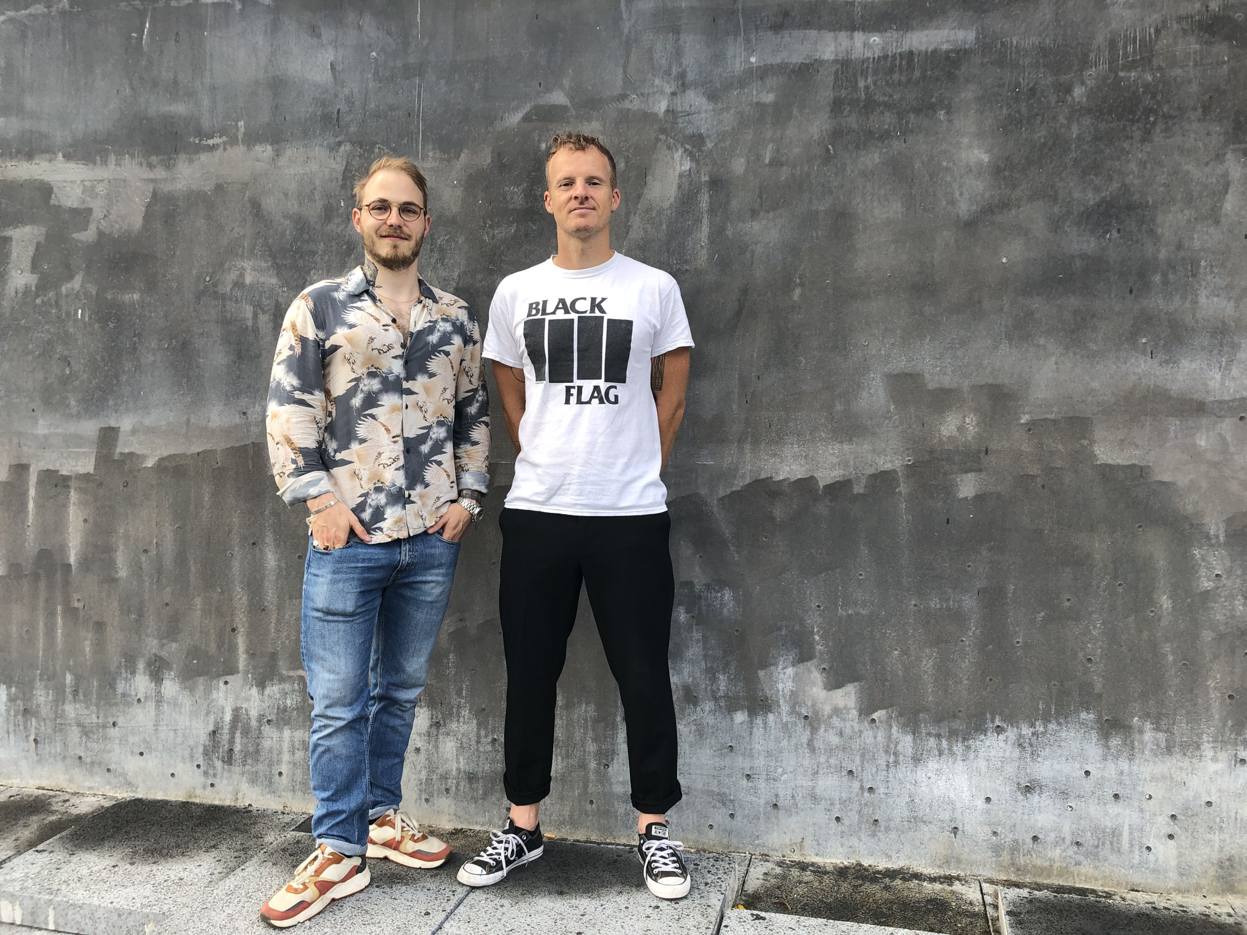 Two men standing up against a wall