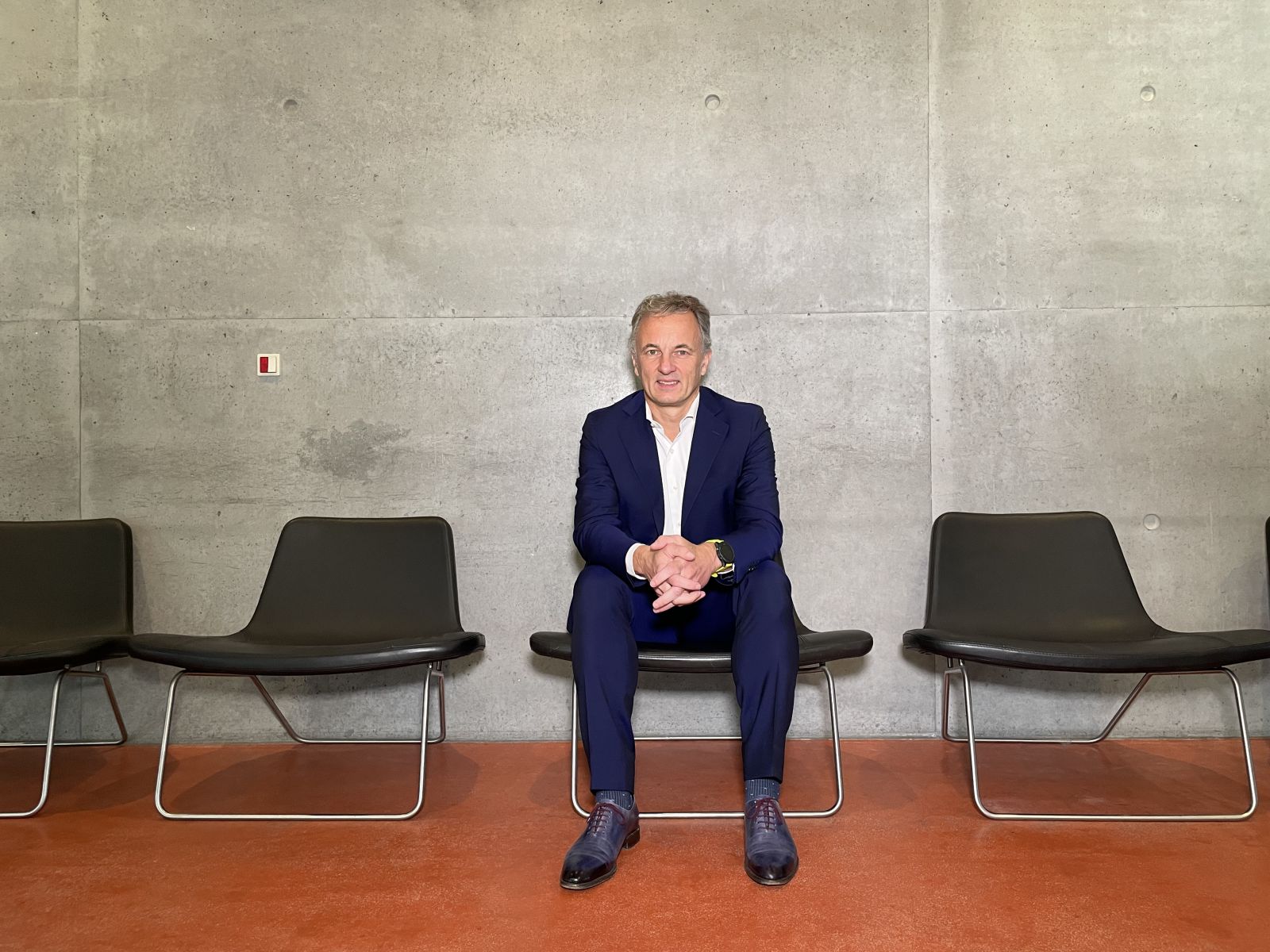 Man in dark blue suit sitting in a black leather chair